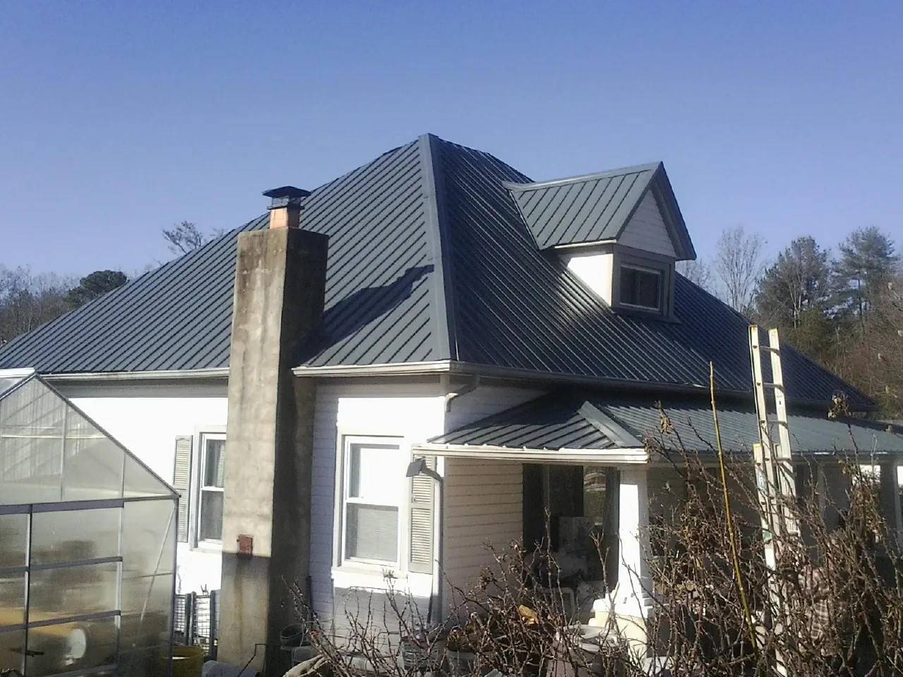 Dark blue standing seam metal roof on a white farmhouse with dormer — Slate & Tile Roof Repair by Roofing Brothers in Wadesboro