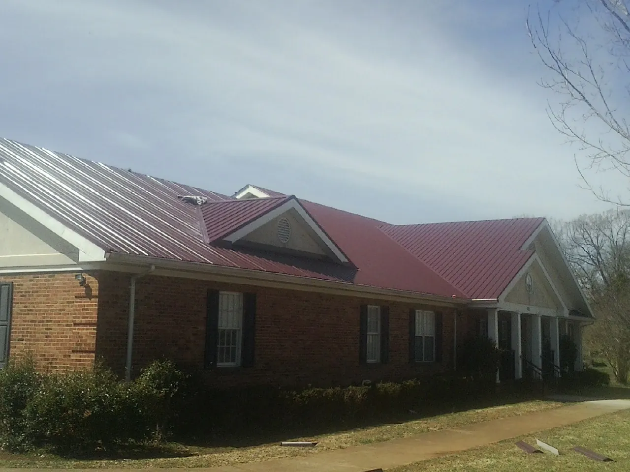 Red metal roof with gabled entries on a long brick building, from a Hail Damage Roof Repair job in Wadesboro