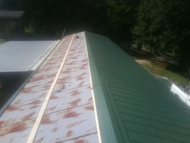 Old rusted panels beside newly installed green metal roofing — Wind Damage Roof Repair by Roofing Brothers in Wadesboro