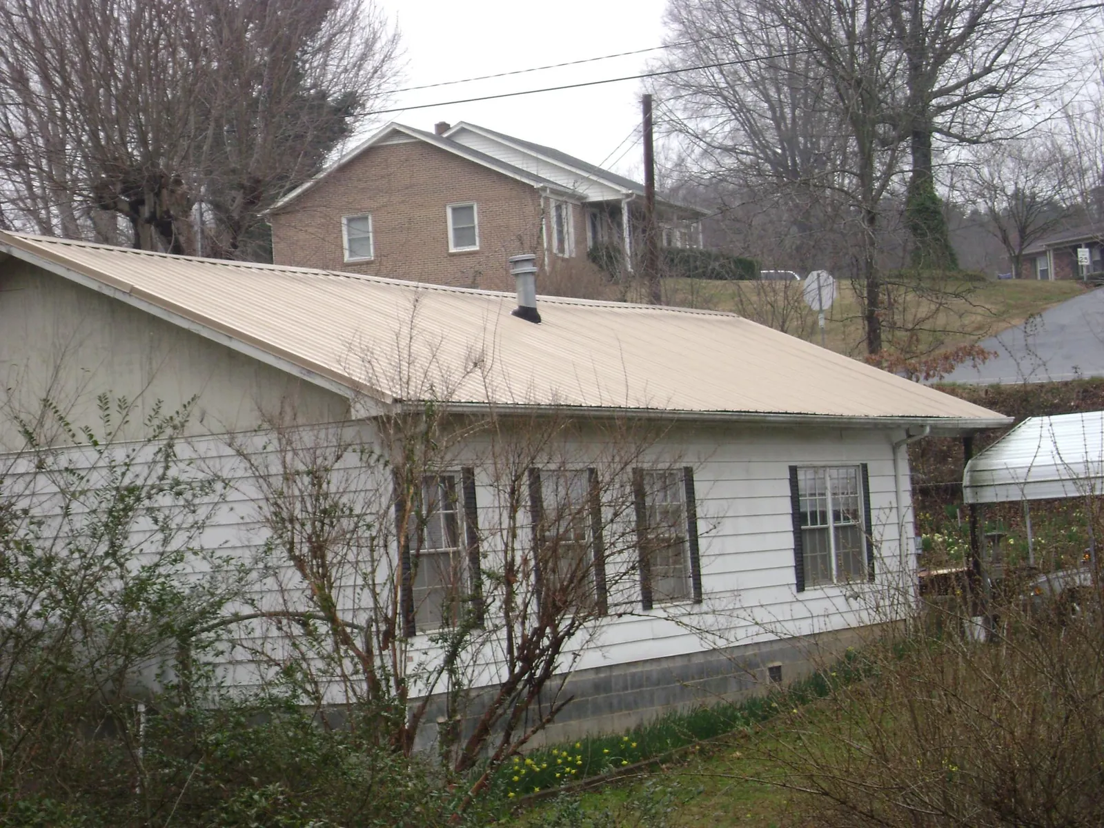 Tan metal roof on a white sided house set into a hillside — Commercial Roofing by Roofing Brothers in Wadesboro