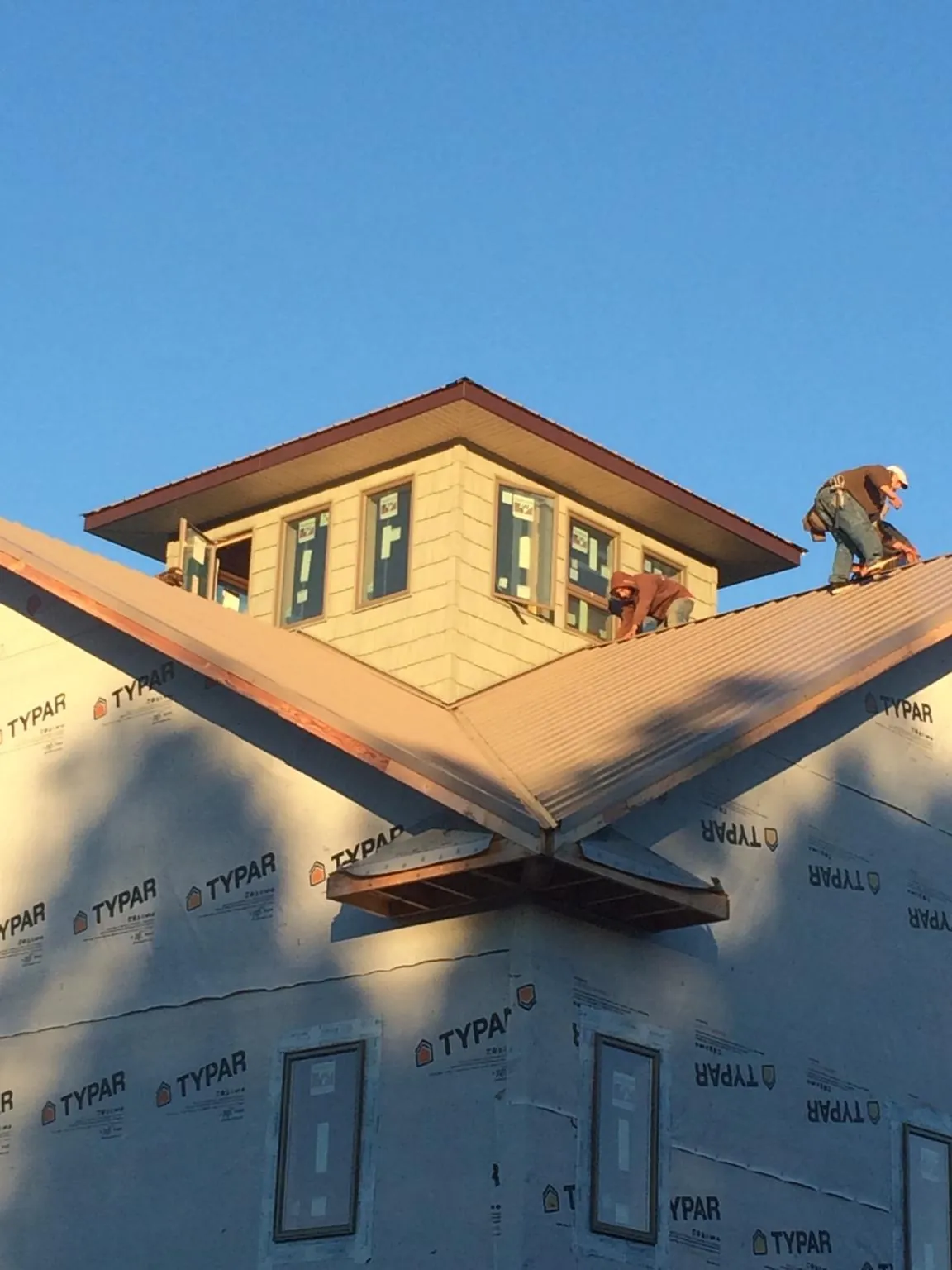 Roofers working around a rooftop cupola on a new metal roof at sunset — Roof Waterproofing in Wadesboro by Roofing Brothers